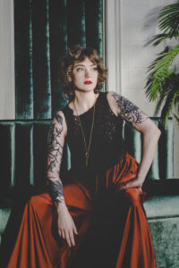 Heidi looks off into the distance as she sits with her hand on her knee. A golden key dangled from a long chain around her neck.