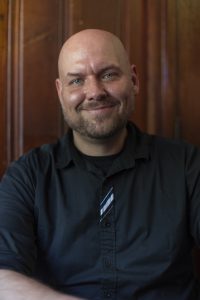 Jeffrey smiles widely at the camera with a tilted, shaved head.